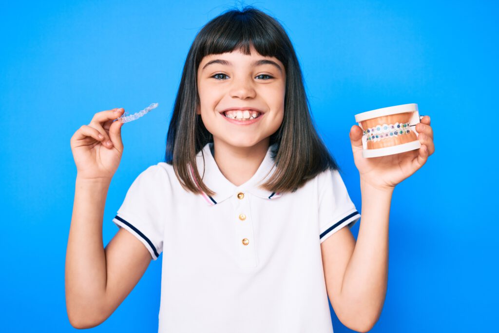 Young little girl with bang holding invisible aligner orthodontic and braces